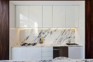 Cocina moderna con gabinetes blancos, salpicadero de mármol y electrodomésticos de acero inoxidable.