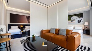 Una habitación de hotel moderna con un sofá de cuero, una cama con ropa blanca, una mesita de noche con una lámpara y un cuadro en la pared.