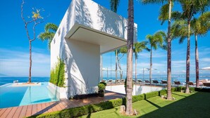 Una villa moderna con piscina, rodeada de palmeras y vista al mar.