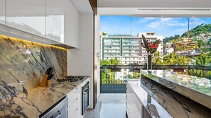 A modern kitchen with a marble countertop, a gas stove, and a view of a cityscape through a balcony. - PIER 57 - 711 | 1BR Penthouse Fabulous Views in PV (Puerto Vallarta)