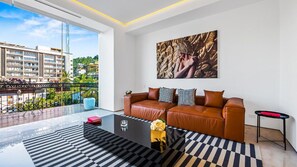 A modern living room with a leather sofa, a glass coffee table, and a large window overlooking a cityscape.