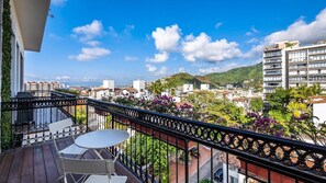 Un balcón con una mesa y sillas, con vistas a un paisaje urbano con edificios y áreas verdes.