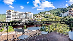 Un balcón con vistas a una colina, un edificio al fondo y una mesa con sillas.