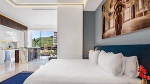 Habitación de hotel moderna con una cama grande, vistas a la ciudad y un área de comedor.