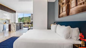 A modern hotel room with a large bed, a view of a cityscape, and a dining area.