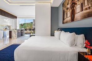Habitación de hotel moderna con una cama grande, vistas a la ciudad y un área de comedor.