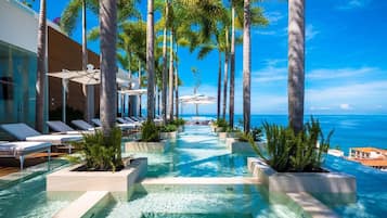 A pool area with lounge chairs and palm trees, leading to a view of the ocean.