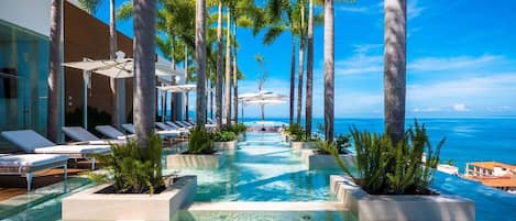 A pool area with lounge chairs and palm trees, leading to a view of the ocean.