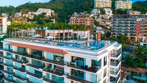 Un hotel de varios pisos con balcones, una piscina en la azotea y vistas a una colina.