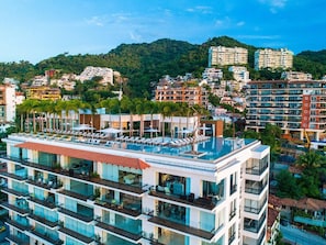 Un hotel de varios pisos con balcones, una piscina en la azotea y vistas a una colina.
