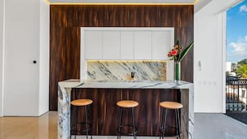 A kitchen with a marble countertop, wooden paneling, and three stools.