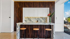 Cozinha com bancada de mármore, painéis de madeira e três banquetas.
