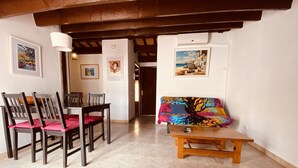 A dining area with a wooden table and chairs, a colorful sofa, and artwork on the walls. - QUIET APARTMENT  (Canet de Mar)