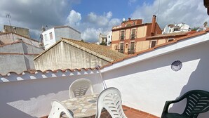 A rooftop terrace with a table and two chairs, a green chair, and a white wall with a decorative plate. - QUIET APARTMENT  (Canet de Mar)