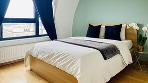 A bedroom with a bed, a window with curtains, a view of buildings, and a potted orchid. - Luxury Green Penthouse Center - Parking (Luxembourg City)