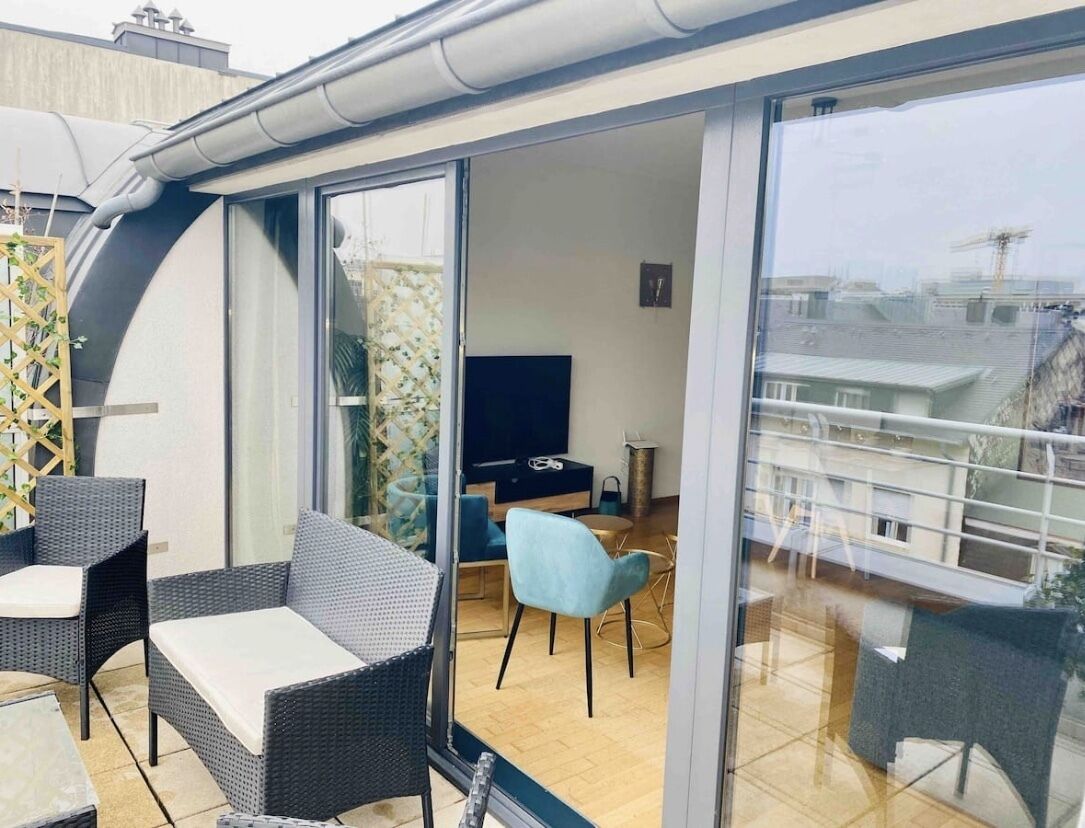 A modern balcony with wicker furniture, a TV, and a dining area.