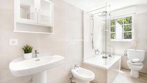 Un baño moderno con lavamanos pedestal, un bidé, ducha con cerramiento de vidrio y un inodoro.