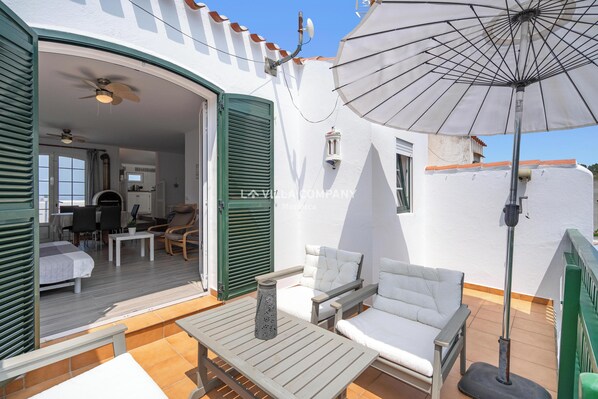 An open patio with outdoor furniture, a ceiling fan, and a white umbrella. - Charming Duplex with Sea Views, 2 Bedrooms + 3 Bathrooms, 3 Minutes to Beach (Arenal d'en Castell, Es Mercadal)