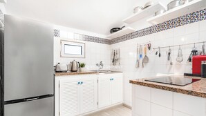 Una cocina moderna con armarios blancos, un refrigerador de acero inoxidable, una encimera con una tetera, un tostador y un lavamanos.