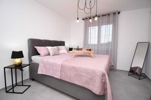 A modern bedroom with a grey bed, a bedside table with a lamp, a bedside table with a tray of toiletries, and a standing mirror. - Brand new top villa ***** heated pool, barbecue, only 2 km from the sea (Pula)