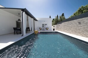 A modern outdoor pool area with a clear blue pool, a covered seating area with chairs, and a stone wall. - Brand new top villa ***** heated pool, barbecue, only 2 km from the sea (Pula)