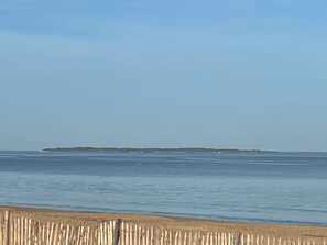 Een strand met een houten hek op de voorgrond en een eiland in de verte.