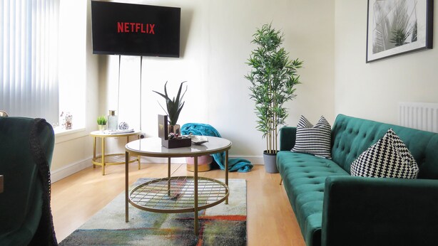Ein Wohnzimmer mit einem grünen Sofa, einem runden Couchtisch und einem Fernseher, der 'NETFLIX' anzeigt.