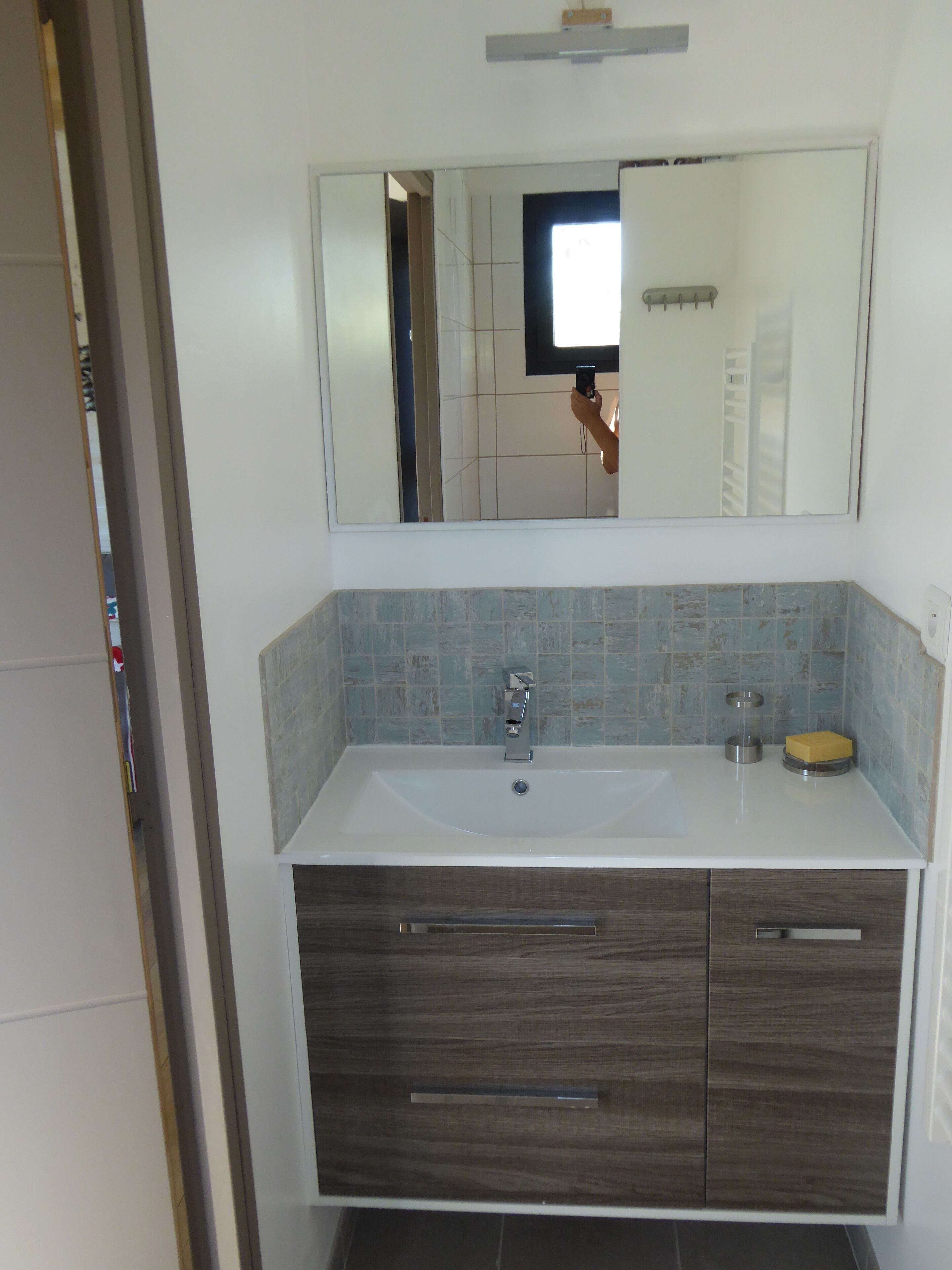 Un baño con lavamanos blanco, tocador de madera oscura y salpicadero de azulejos.
