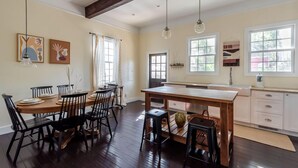 A spacious dining area with a wooden table and chairs, a kitchen with white cabinets, and large windows allowing natural light. - Bright Bohemian Home w/ Parking + Deck Near Forsyth Park by Lucky Savannah (Savannah)