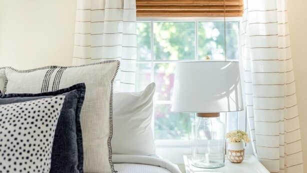 A neatly made bed with white and patterned pillows, a bedside lamp, and a small vase with flowers on a bedside table. - Bright Bohemian Home w/ Parking + Deck Near Forsyth Park by Lucky Savannah (Savannah)