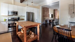 A modern kitchen with white cabinets, stainless steel appliances, and a wooden island table. - Bright Bohemian Home w/ Parking + Deck Near Forsyth Park by Lucky Savannah (Savannah)