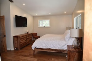 Een slaapkamer met een bed, een houten dressoir, een televisie, een raam en een lamp.