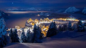 A snow-covered landscape with a town illuminated by lights, surrounded by snow-covered trees and mountains in the background. - Apt, 1206 _ Properties Mont Amour  (Morzine)