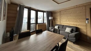 A modern room with a wooden floor, a dining table with chairs, a sofa, and a window with curtains. - Apt, 1206 _ Properties Mont Amour  (Morzine)