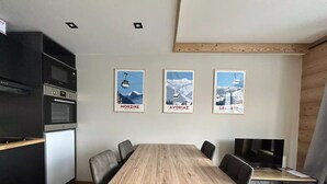A modern kitchen with a dining area, featuring a wooden table and chairs, a built-in oven, and a TV on a wooden stand. - Apt, 1206 _ Properties Mont Amour  (Morzine)