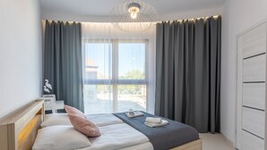 Een moderne slaapkamer met een houten bed, grijze gordijnen en uitzicht op het omliggende landschap.