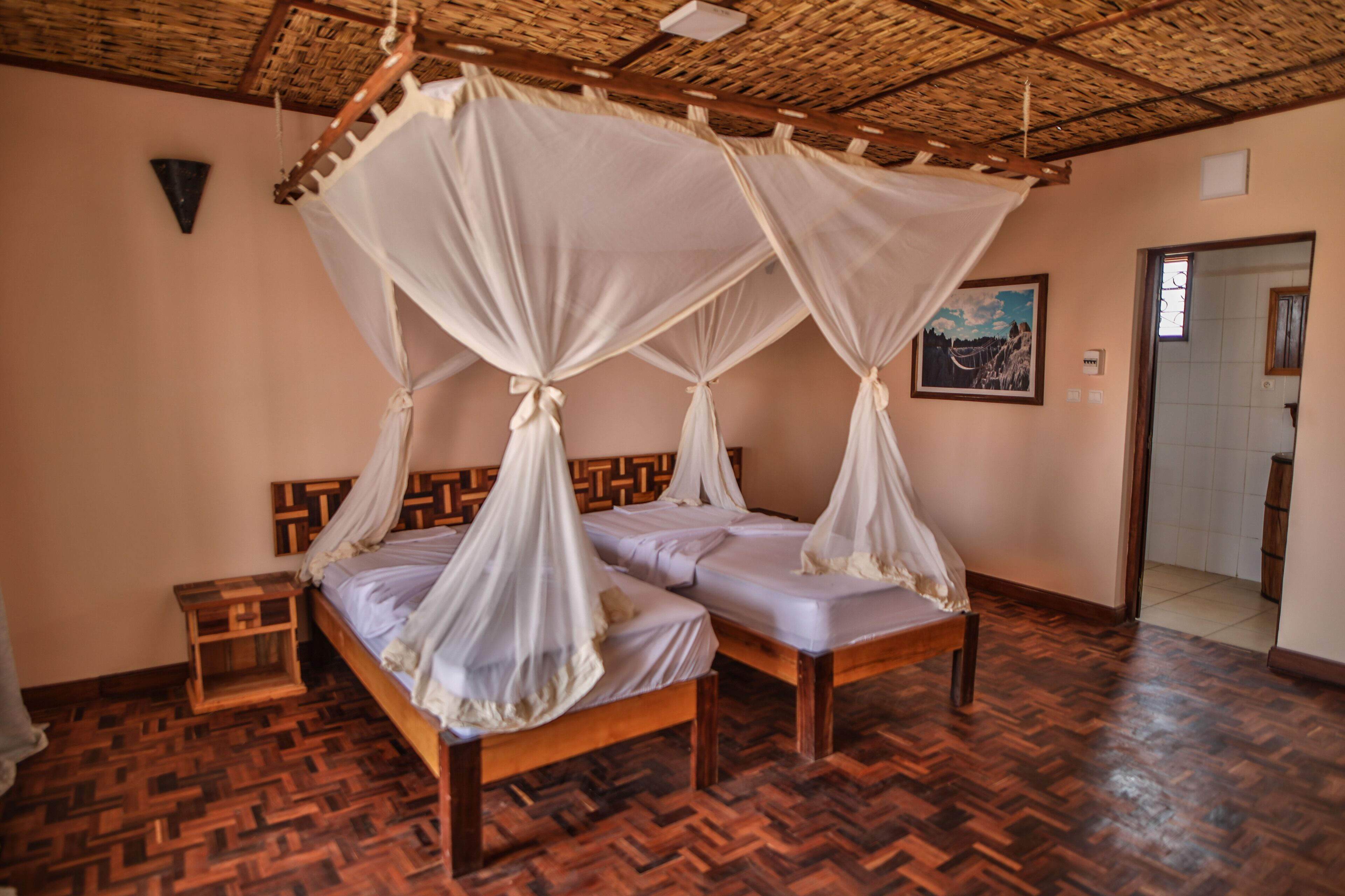 A room with two wooden beds, each with a canopy. There is a wooden headboard, a small wooden nightstand, and a framed picture on the wall.