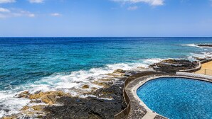 Una piscina junto a una costa rocosa con el océano al fondo.