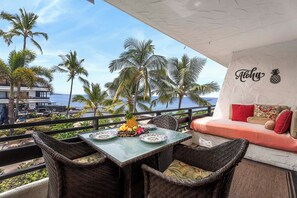 Een balkon met rieten meubilair, een tafel met borden en een fruitmand, en een muur met een ananas logo.