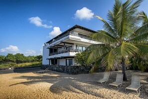 Een tweelaags pand aan het strand met een balkon, een stenen muur en een palmboom.
