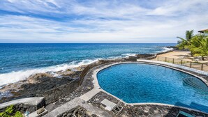Una piscina circular con vistas al océano y una zona de playa con palmeras.