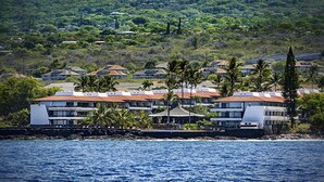 Un hotel costero con varias construcciones, palmeras y vista al océano.