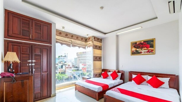 Ein Hotelzimmer mit zwei Betten, einem Schreibtisch und einem großen Fenster mit Blick auf die Stadt.