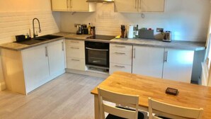 Une cuisine moderne avec des meubles blancs, un four encastré, un évier et une table à manger en bois avec des chaises.