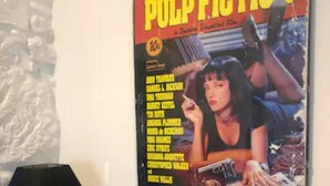 Une affiche du film « Pulp Fiction » accrochée au mur, une lampe noire et un présentoir à magazines rempli de livres.