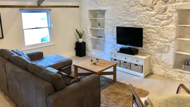 Un salon avec un mur en pierre, un canapé, une table basse et un téléviseur.