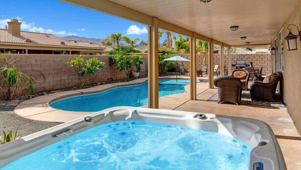 A covered outdoor area with a hot tub, a swimming pool, and outdoor furniture.