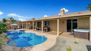 A swimming pool with a curved edge, a covered patio area with outdoor furniture, and a hot tub.