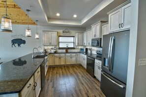 A modern kitchen with light wooden cabinets, stainless steel appliances, and a black granite countertop.