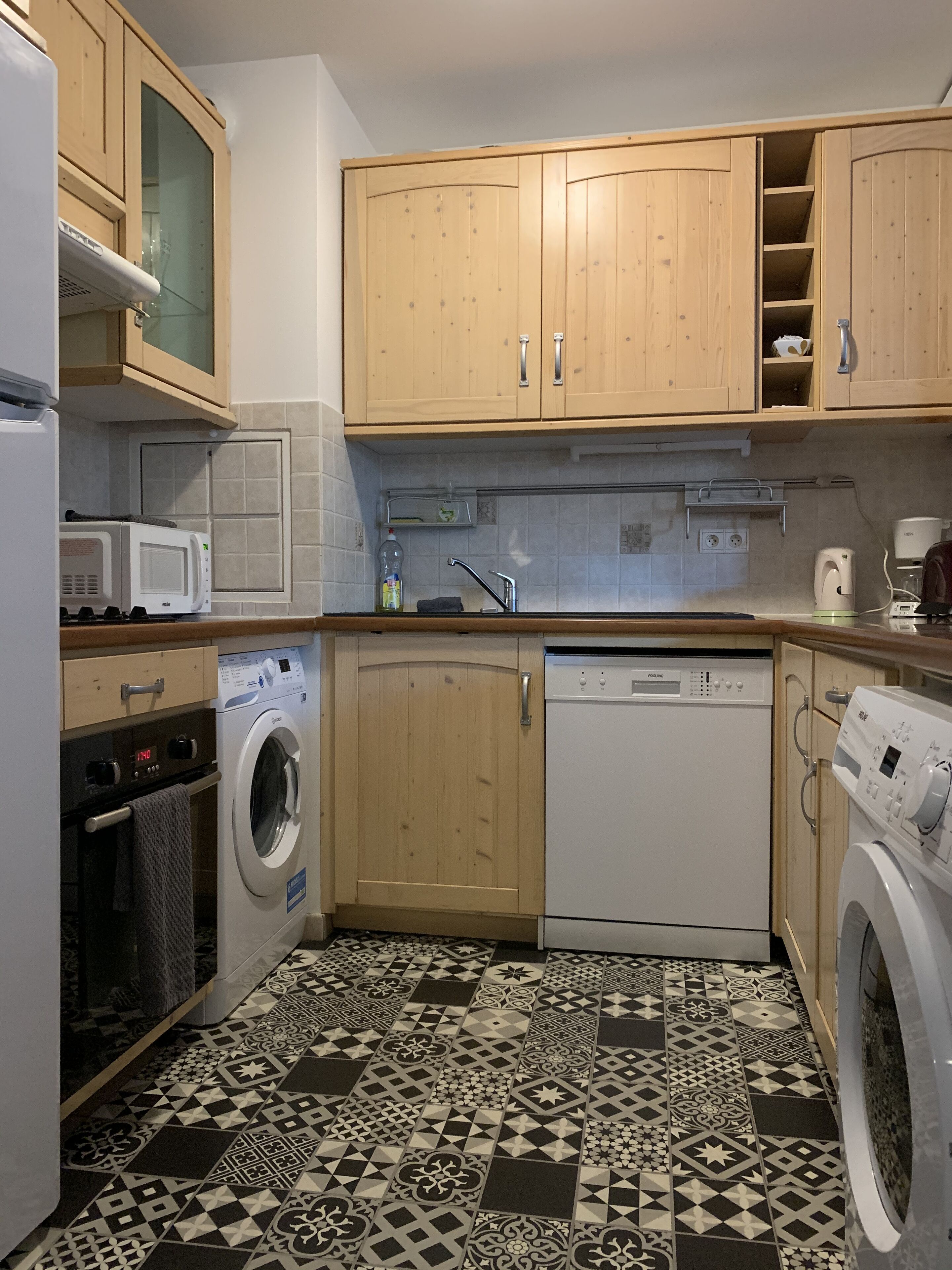 A compact kitchen with wooden cabinets, a washing machine, a dishwasher, and a microwave.